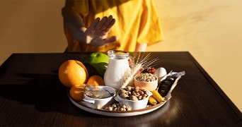 Allergenen concept met handgebaar, diverse voedingsmiddelen zoals melk, noten, en zeevruchten op een tafel.