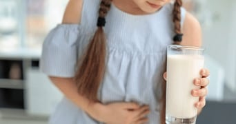 Meisje met vlechten houdt glas melk vast en heeft buikpijn.