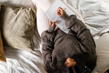 Vrouw die notities maakt op een bed met meerdere kussens, gezien van bovenaf.