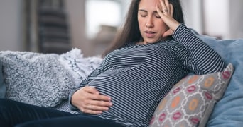 Vrouw die misselijk op de bank zit.
