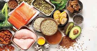 Gezonde voedingsmiddelen zoals zalm, kipfilet, avocado, amandelen en groenten op een tafel.