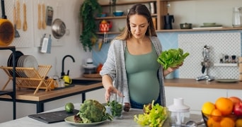 Zwangere vrouw in een keuken die verse groenten op het aanrecht klaarmaakt