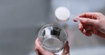 Handen houden een glas water en een schepje wit poeder.