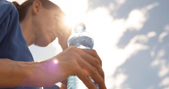 Persoon die een fles water vasthoudt tegen de zonsondergang.