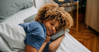 Persoon met krullend haar liggend op bed onder een deken