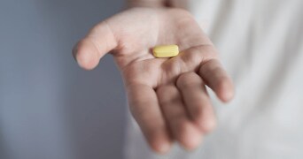 Menselijke hand met een gele pil.