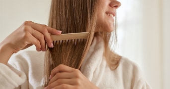 Vrouw kamt lang bruin haar met een houten kam terwijl ze een badjas draagt