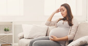 Zwangere vrouw zittend op een lichte bank in een huiselijke woonkamer