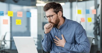 Man houdt zijn borst vast terwijl hij achter een laptop zit.