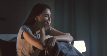 Vrouw zittend op bed in kamer met nachtlampje.