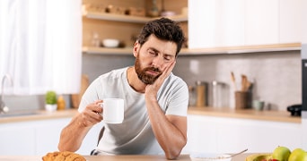 Man die moe is na het opstaan met een kop koffie in zijn handen.