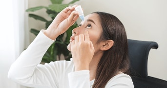 Vrouw die oogdruppels gebruikt in een thuiskantooromgeving