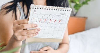 Vrouw houdt een kalender vast met rode vraagtekens op bepaalde datums in augustus 2021.