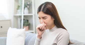 Vrouw met lang bruin haar zittend op een bank in een licht ingerichte woonkamer