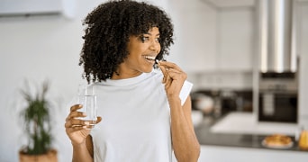 Persoon in witte trui houdt een glas water vast in een moderne keuken.