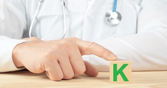 Arts in witte jas wijst naar een houten blok met een groene letter K.