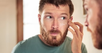 Man met een lichtgroene trui die zich aan het oor raakt binnenshuis