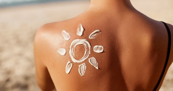 Zonnebrandcrème in de vorm van een zon op een rug op het strand.