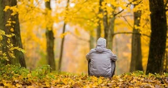 Persoon met een grijze jas zit in een herfstbos met gele bladeren