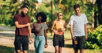 Vier mensen wandelen buiten in een park en dragen drankjes in hun hand
