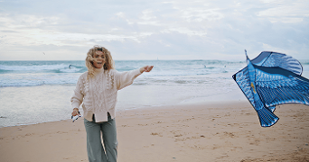 Persoon laat een blauwe vlieger op op een zandstrand met zee op de achtergrond.