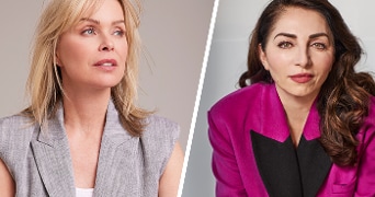 Twee vrouwen in professionele kleding, één in een grijs jasje en de ander in een roze blazer.