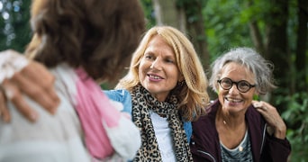 Drie vrouwen in een bosomgeving, waarbij twee vrouwen elkaar omhelzen.