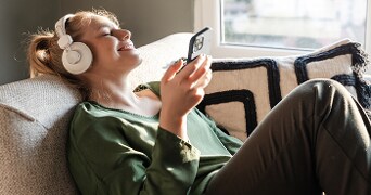 Persoon in groene trui met hoofdtelefoon ontspant op de bank met smartphone in hand
