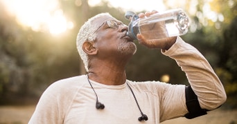 Persoon drinkt water uit een fles tijdens het sporten buiten.