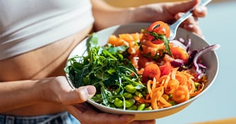 Salade met rucola, cherrytomaten, wortel en sojabonen in een kom, in een hand gehouden.