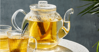 Glazen theepot gevuld met warme thee, citroen en een kaneelstokje, geserveerd met twee glazen op een tafel