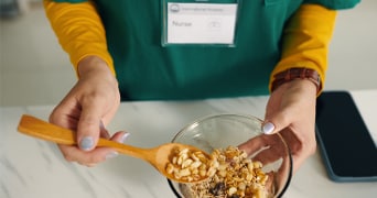 Persoon in verpleegkundige uniform schept muesli met noten in een glazen kom met een houten lepel