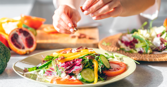 Verse salade met tomaat, komkommer, gele paprika, gemengde sla en noten, terwijl iemand noten toevoegt aan het bord.