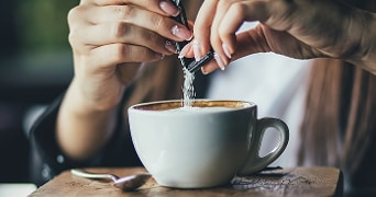 Persoon voegt suiker toe aan een kop cappuccino.