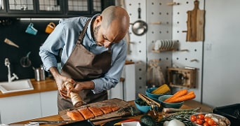 Man in schort die zalm prepareert in een keuken met verse groenten zoals wortels en tomaten.
