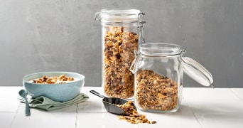 Knapperige muesli in glazen potten naast een kom yoghurt.