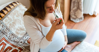 Zwangere vrouw zit op bed en kijkt naar een thermometer.