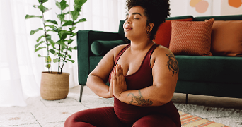 Person in yoga pose wearing a maroon outfit in a living room with plants and a couch.