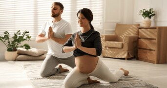 Zwanger koppel beoefent yoga in een woonkamer.