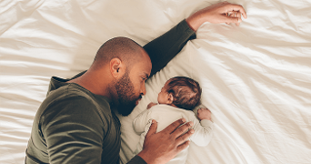 Vader knuffelt zijn slapende baby op bed.