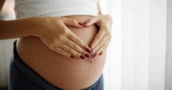 Zwangere vrouw houdt handen in hartvorm op haar buik.