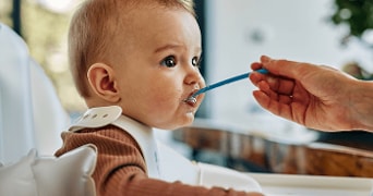 Een hand voedt een baby met een blauwe lepel.