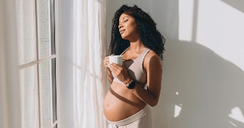 Zwangere vrouw geniet van een drankje bij het raam, gezicht is onscherp gemaakt.