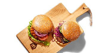 Twee hamburgers met verschillende groentes op een houten serveerplank