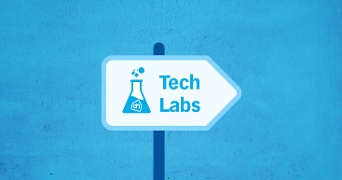 Wegwijzer met laboratoriumfles en tekst "Tech Labs" op blauwe achtergrond, met AH-logo in de fles.