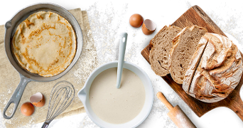 Ingrediënten en bakbenodigdheden voor het maken van pannenkoeken en brood: pannenkoek in een koekenpan, beslag in een kom, eieren en gesneden brood.