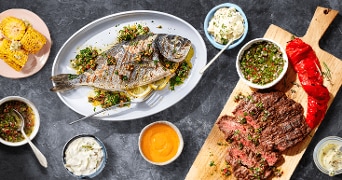 Gegrilde vis en steak geserveerd met sauzen en gegrilde maïs.