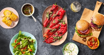 Culinaire barbecue opstelling met gegrilde maiskolven, salade, gepofte rode paprika's, hamburgers en yoghurtsaus.