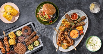 Barbecue maaltijd met gegrilde maïs, hamburger en diverse vleesspiezen op een tafel.