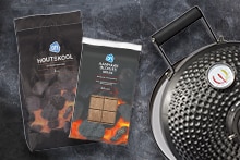 Zak AH houtskool, verpakking AH aanmaakblokjes bruin en het deksel van een barbecue met temperatuurmeter.